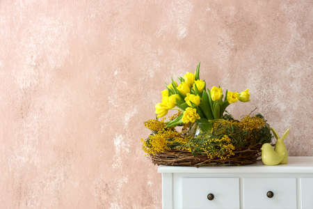 Nest with beautiful flowers and Easter decor on table near color wallの写真素材