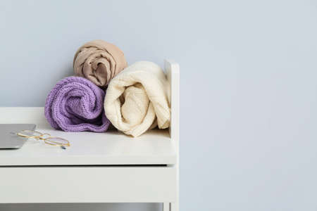 Folded sweaters with eyeglasses on table near light wallの写真素材