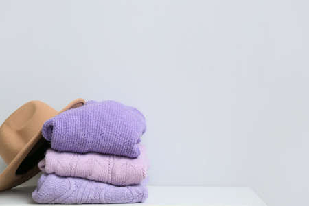 Stack of knitted sweaters and hat on table near light wallの写真素材