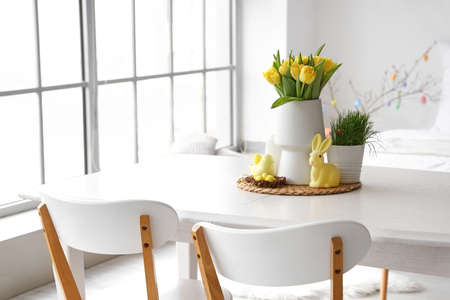 Vase with tulips, Easter eggs and decor on dining table in room