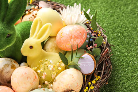Nest with painted Easter eggs, bunnies and flowers on green background, closeup