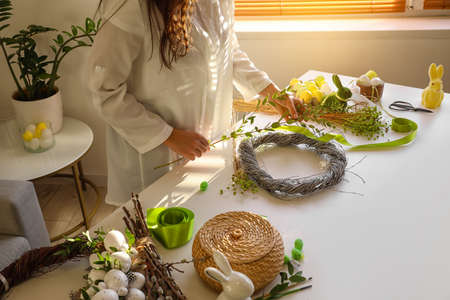 Woman making beautiful Easter wreath at table, closeup
