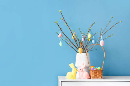 Vase with tree branches, Easter eggs in basket and rabbits on chest of drawers near color wallの写真素材