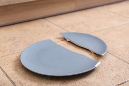 Broken gray ceramic plate on floor in kitchen, closeupの写真素材