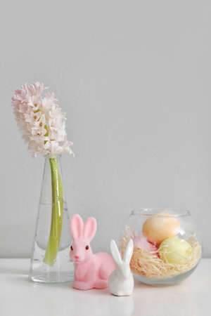 Vase with hyacinth flower, Easter eggs and rabbits on table near light wallの写真素材