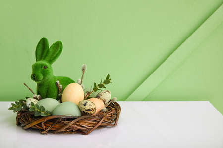 Nest with Easter eggs, rabbit and eucalyptus branches on table near color wallの写真素材