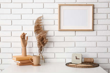 Workplace with wooden hand, books, cup, pampas grass in vase and clock near white brick wallの写真素材