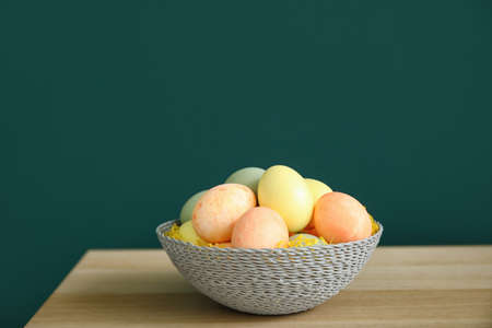 Bowl with Easter eggs on table near dark wall