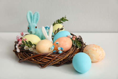 Nest with Easter eggs, rabbits and gypsophila flowers on table near light wall