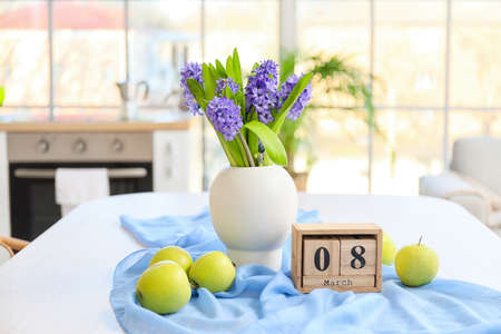 Vase with flowers, fresh apples and cube calendar with date 8 MARCH on dining table. International...