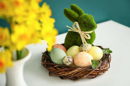 Nest with Easter eggs, rabbit and narcissus flowers on table near dark wall, closeupの写真素材