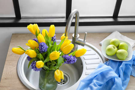 Vase with flowers in sink and fresh apples on kitchen counterの写真素材
