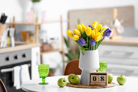 Cube calendar with date 8 MARCH, fresh apples, flowers and glasses on dining table. International...