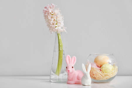 Vase with hyacinth flower, Easter eggs and rabbits on table near light wallの写真素材
