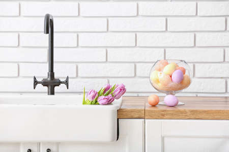 Tulips in sink and Easter eggs on kitchen counter near white brick wallの写真素材