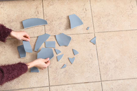 Female hands with broken ceramic plate on color tileの写真素材