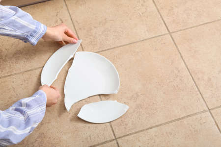 Female hands with broken white plate on color tile