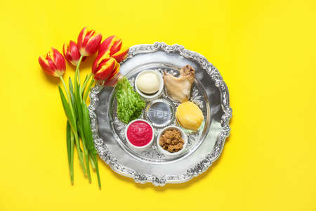 Passover Seder plate with traditional food and tulip flowers on color backgroundの写真素材