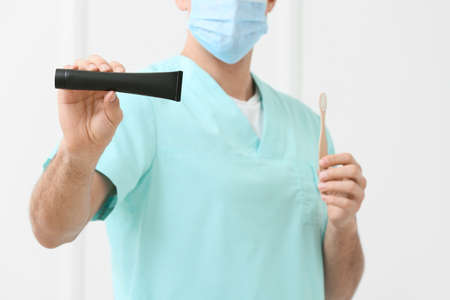 Male dentist with activated charcoal tooth paste and brush on light background, closeupの写真素材