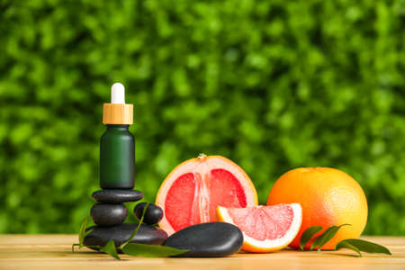 Composition with bottle of essential oil, grapefruit and spa stones on table outdoors