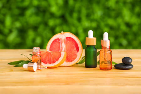 Bottles of essential oil and grapefruit on wooden table outdoors
