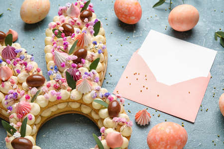 Beautiful cake, painted eggs and envelope for Easter celebration on color background, closeup