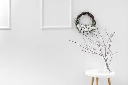 Tree branches in vase on table near white wall with Easter wreathの写真素材