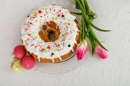 Plate with tasty Easter cake, eggs and flowers on light background