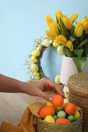 Woman putting Easter eggs into basket on table, closeup