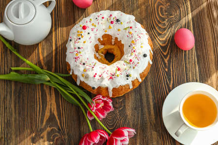 Tasty Easter cake with eggs, flowers and cup of tea on wooden background