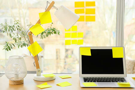 Laptop with sticky notes and lamps on table near window