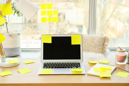Laptop with sticky notes and notebook on table near windowの写真素材