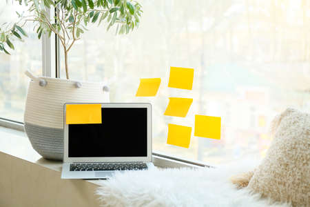 Laptop with sticky notes and houseplant on windowsillの写真素材