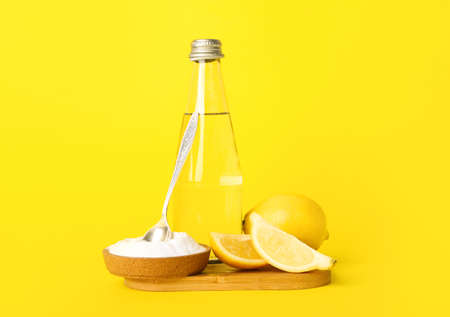 Wooden board with bottle of water, lemon and baking soda on yellow backgroundの写真素材