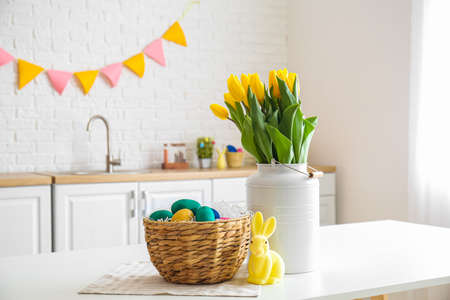 Wicker basket with Easter eggs, rabbit and bouquet of tulips on dining table in kitchenの写真素材