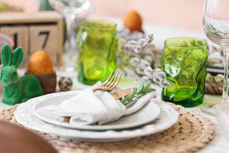 Plates with cutlery and eucalyptus branch on table served for Easter celebration