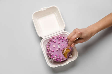 Woman eating tasty bento cake in plastic lunch box on gray background