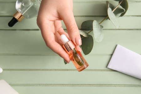 Female hand with bottle of natural serum on color wooden background, closeup