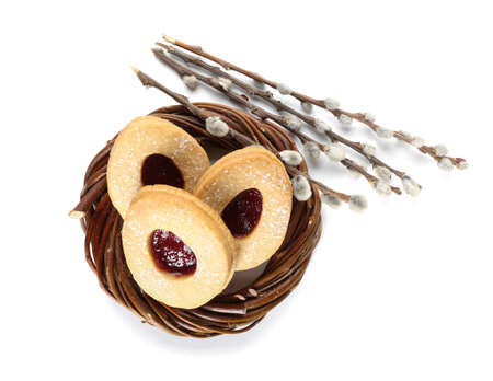 Nest with delicious Easter cookies and willow branches on white background