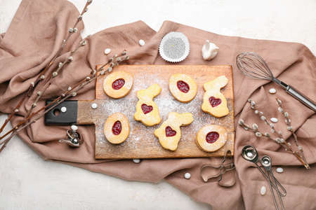 Board with delicious Easter cookies and willow branches on light background
