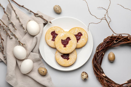 Plate with delicious Easter cookies, eggs and willow branches on light backgroundの写真素材