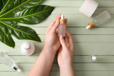 Female hands with bottle of natural serum and cosmetics on color wooden backgroundの写真素材
