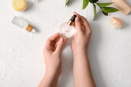 Female hands with bottle of natural serum and cosmetics on light background