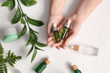 Female hands with bottles of natural serum, cosmetics and plant branch on light backgroundの写真素材