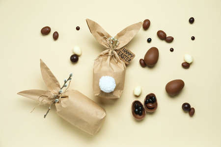 Composition with Easter bunny gift bags and chocolate eggs on color background