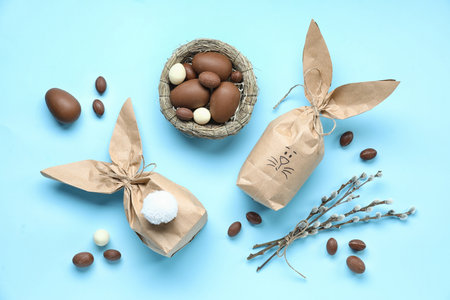 Composition with Easter bunny gift bags, chocolate eggs and pussy willow branches on color...