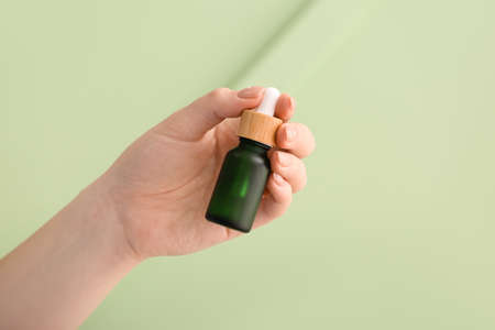 Woman holding bottle of serum against green background, closeupの写真素材