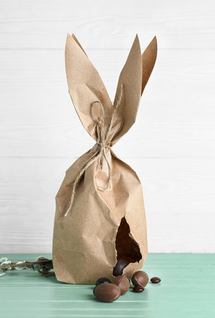 Easter bunny gift bag with chocolate eggs on color wooden table