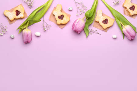 Delicious Easter cookies and flowers on purple background