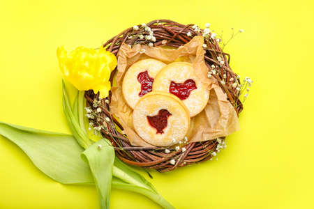 Nest with delicious Easter cookies on yellow background